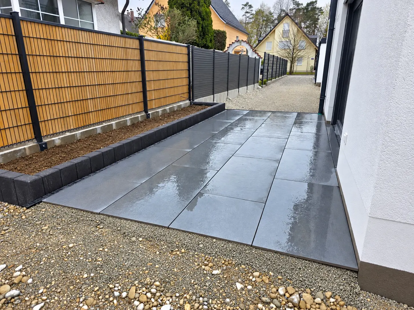Großformatige dunkelgraue Terrassenplatten mit Beeteinfassung und Sichtschutz in München-Aubing