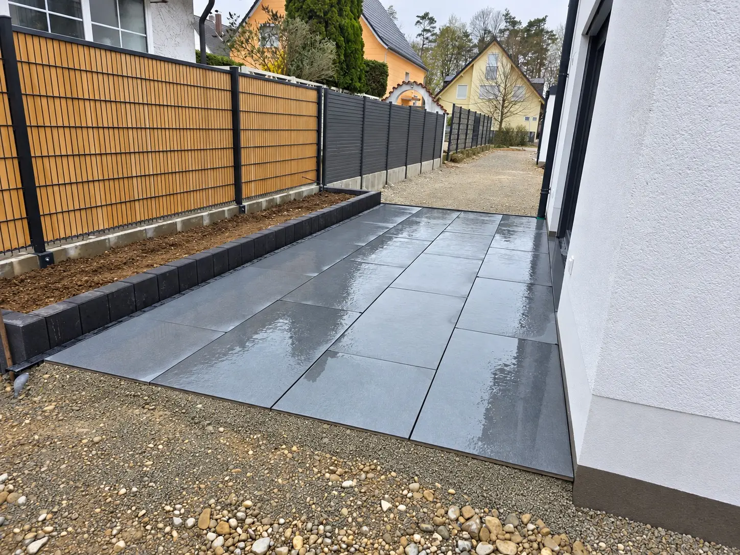 Seitliche Ansicht der neu verlegten Terrasse mit dunklen Platten und eingefasstem Beet in München-Aubing
