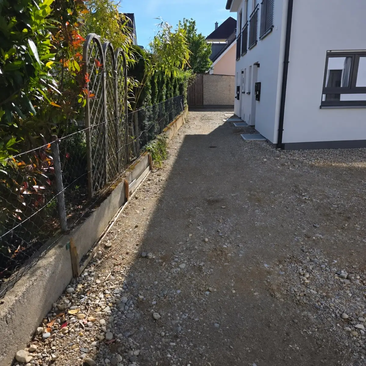 Unbefestigte Zufahrt mit altem Zaun und Betonrand vor der Neugestaltung in München-Aubing