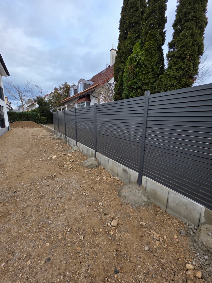 Innenseite des Sichtschutzzauns mit Betonunterbau und sichtbaren Pfostenfundamenten in München