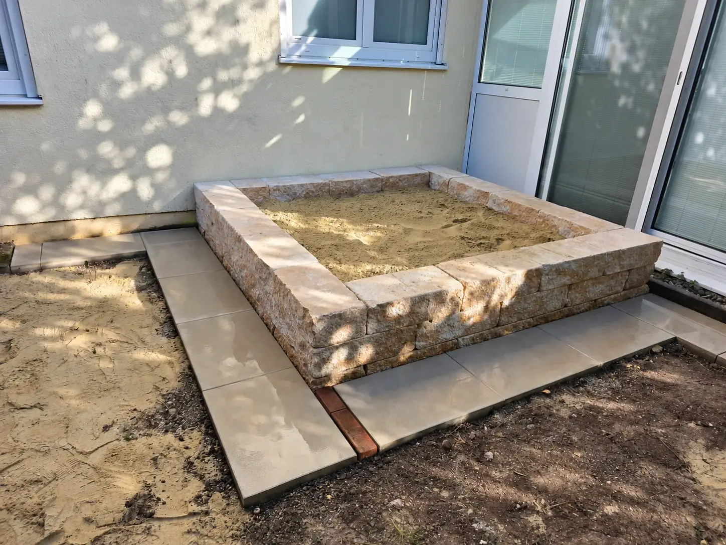 Mit Sand gefüllter Sandkasten mit neuer Platteneinfassung vor Fertigstellung der Rasenfläche