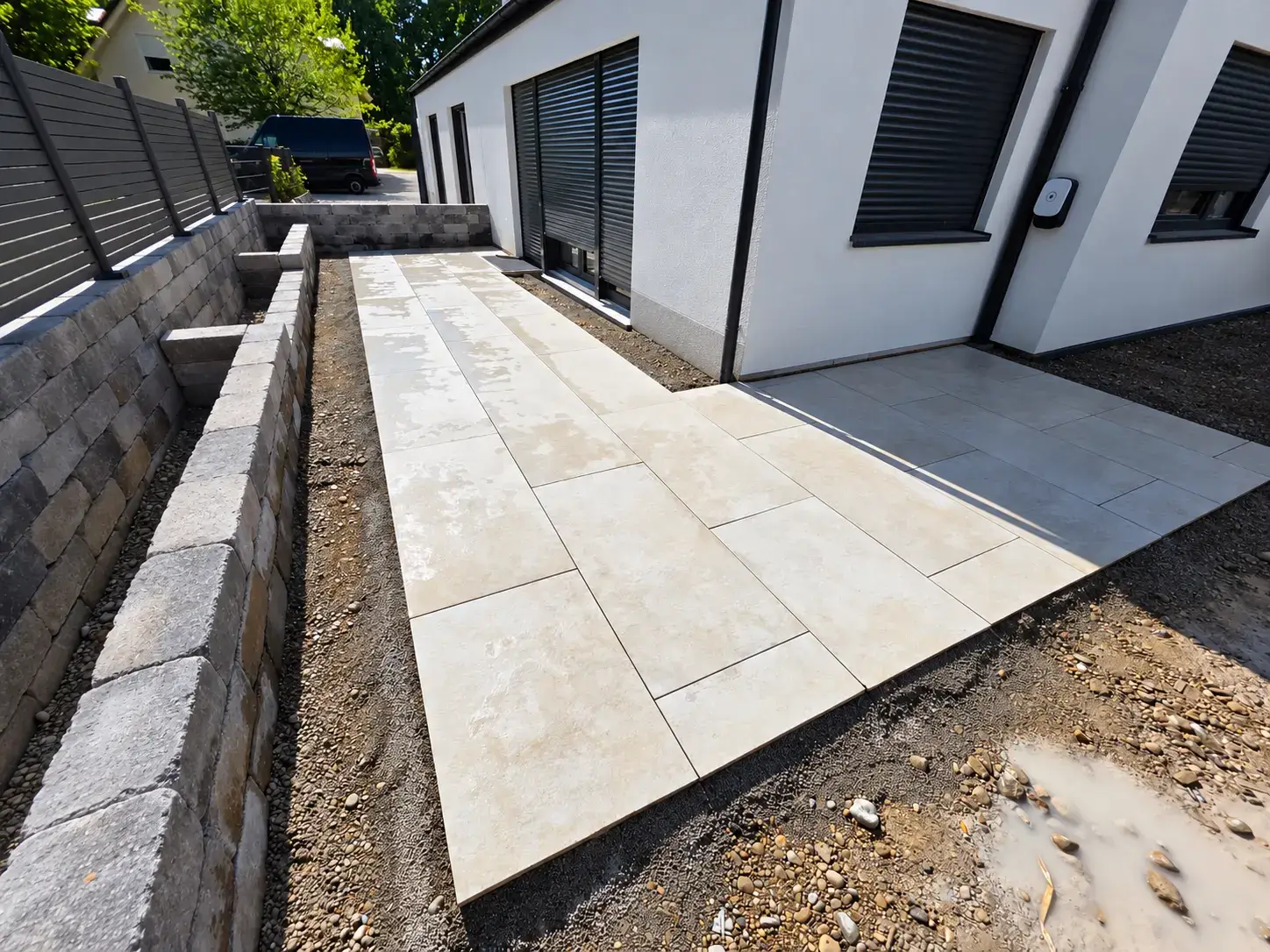 Bauphase beim Verlegen großformatiger Terrassenplatten zwischen Haus und Pflanzmauer